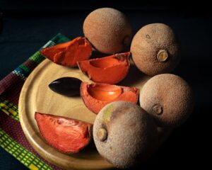 Close-up of fresh mamey sapote fruit sliced on a wooden tray, showcasing its vibrant color.