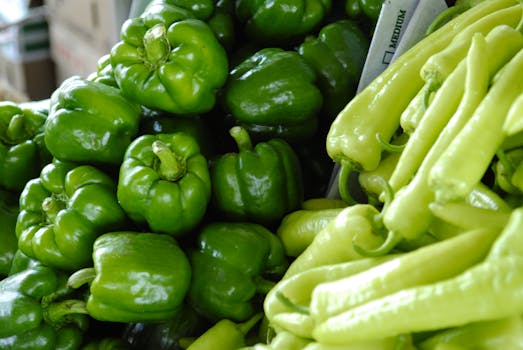 Close-up of fresh green bell peppers and chili peppers, showcasing vibrant and organic produce in a market setting.